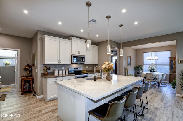 kitchen with pendant lighting, white cabinets, stainless steel appliances, an island with sink, and sink