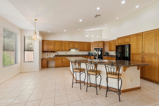 kitchen with an inviting chandelier, a center island with sink, black appliances, a kitchen bar, and dark stone countertops