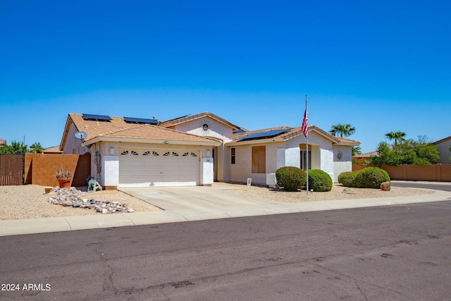 view of front of house with an attached garage, solar panels, fence, and concrete driveway