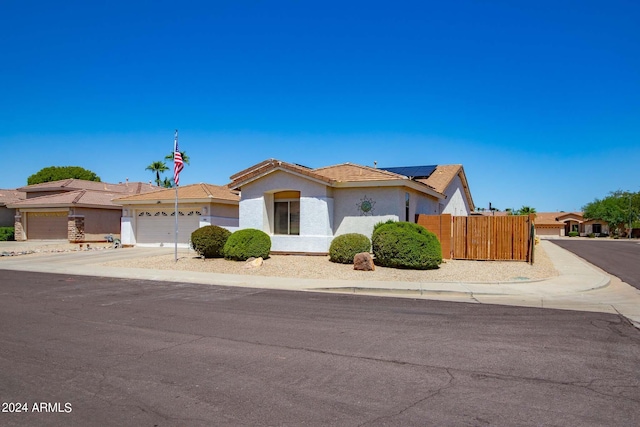 view of front of house with stucco siding, concrete driveway, roof mounted solar panels, fence, and a garage