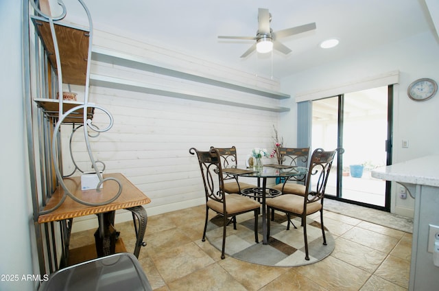 dining space with ceiling fan, wooden walls, and baseboards