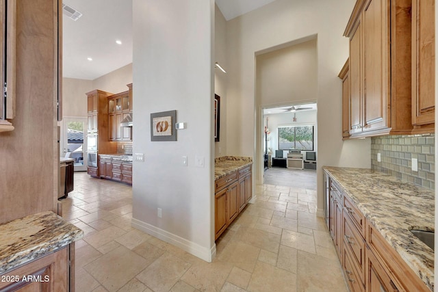 kitchen with ceiling fan, range hood, light stone counters, and tasteful backsplash