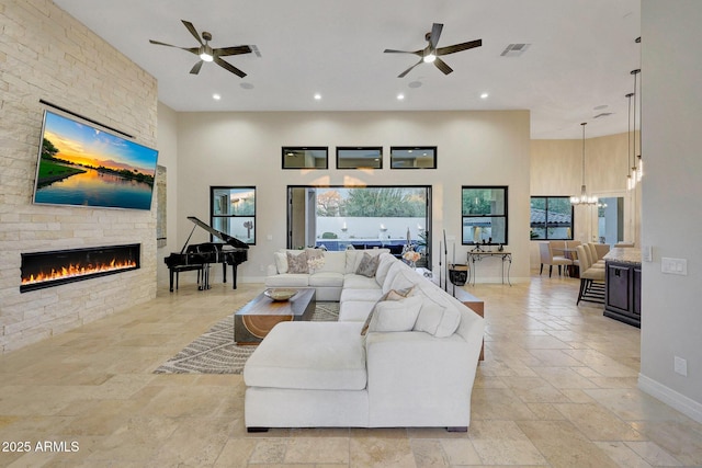 living room with a high ceiling, ceiling fan with notable chandelier, and a fireplace