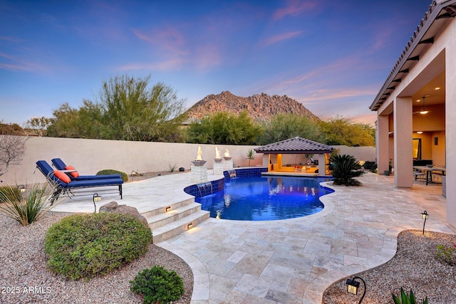 pool at dusk with a patio area, a mountain view, and a gazebo