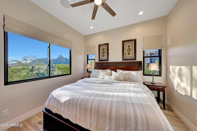 bedroom featuring ceiling fan, light hardwood / wood-style floors, multiple windows, and a mountain view