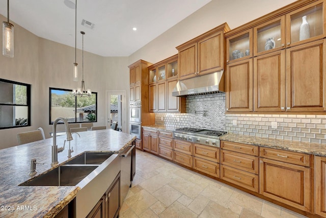 kitchen featuring appliances with stainless steel finishes, hanging light fixtures, light stone countertops, decorative backsplash, and sink