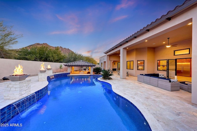 pool at dusk featuring an outdoor living space with a fire pit, a patio, pool water feature, and a gazebo