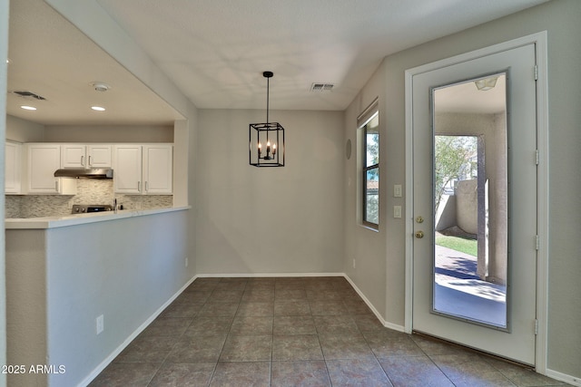 unfurnished dining area featuring a chandelier, dark tile patterned flooring, visible vents, and baseboards