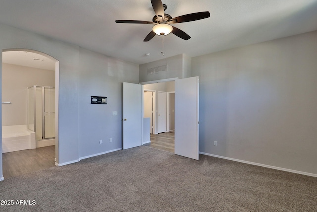 unfurnished bedroom with baseboards, visible vents, connected bathroom, arched walkways, and carpet flooring