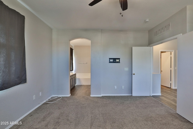 unfurnished bedroom featuring baseboards, arched walkways, connected bathroom, ceiling fan, and carpet