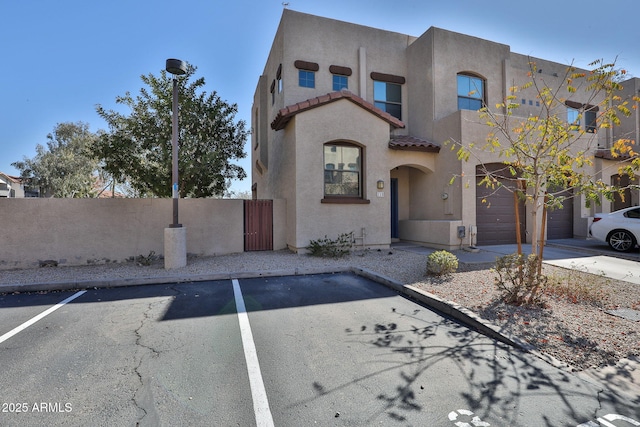 view of front of home with uncovered parking, a tiled roof, fence, and stucco siding