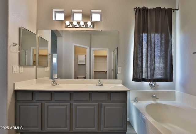 bathroom with a sink, double vanity, a garden tub, and a textured wall