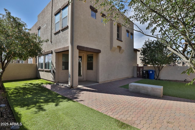 rear view of property featuring a patio, a yard, fence, and stucco siding