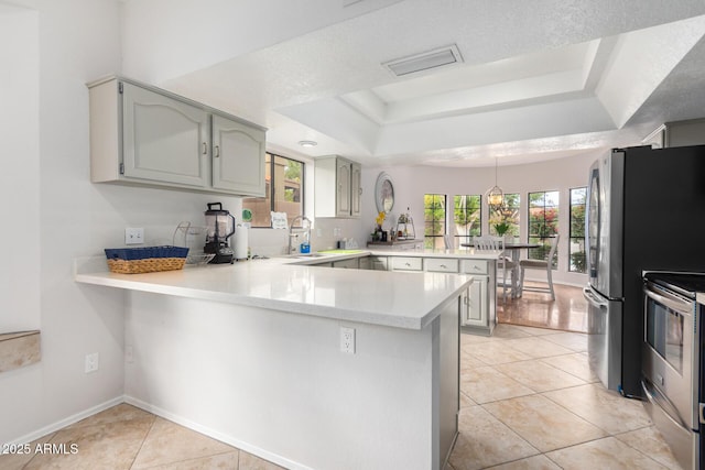 kitchen with stainless steel appliances, light tile patterned flooring, a raised ceiling, and kitchen peninsula