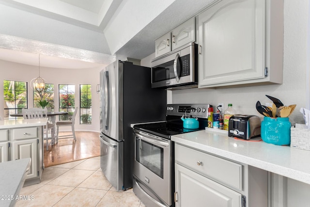 kitchen with pendant lighting, a notable chandelier, white cabinetry, appliances with stainless steel finishes, and light tile patterned flooring