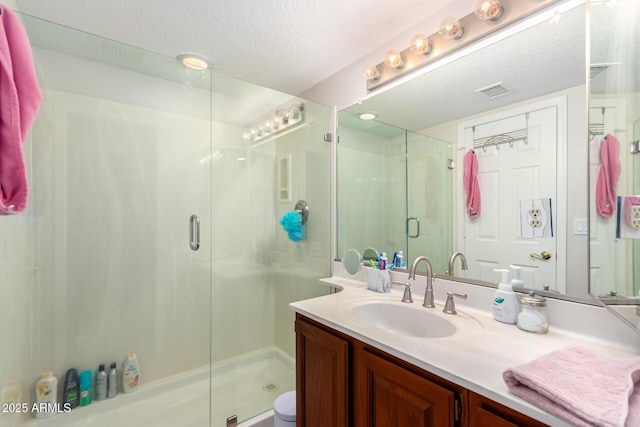 bathroom with a textured ceiling, vanity, and a shower with shower door