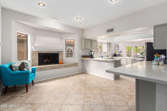 kitchen with kitchen peninsula, gray cabinetry, stainless steel refrigerator, a fireplace, and light tile patterned flooring