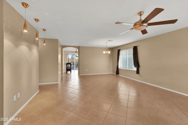 empty room featuring light tile patterned flooring, baseboards, arched walkways, and ceiling fan with notable chandelier