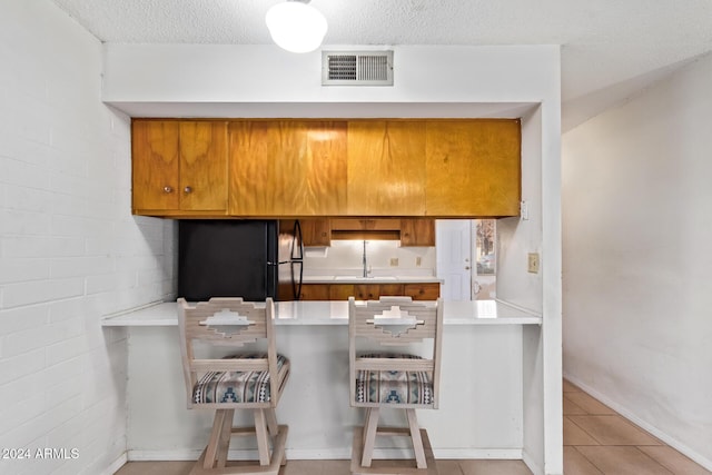 kitchen with kitchen peninsula, black refrigerator, light tile patterned floors, and a textured ceiling