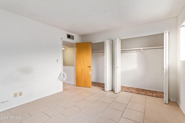 unfurnished bedroom with a textured ceiling, light tile patterned flooring, and two closets