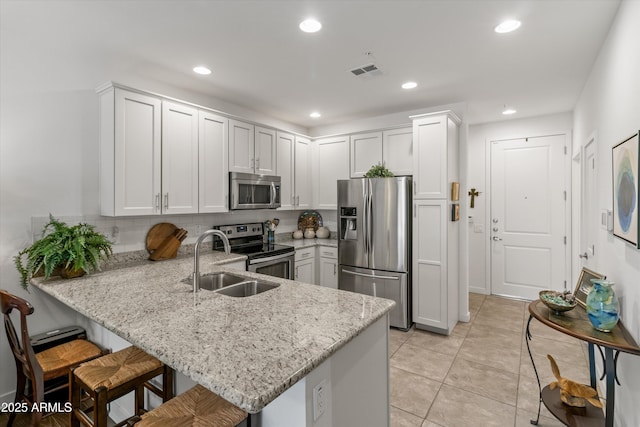 kitchen with kitchen peninsula, stainless steel appliances, sink, white cabinets, and a breakfast bar area