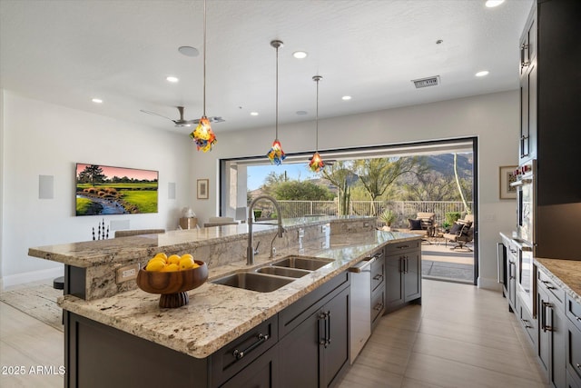 kitchen with oven, light stone countertops, recessed lighting, a sink, and a large island with sink