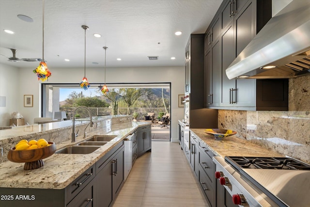 kitchen featuring decorative backsplash, visible vents, wall chimney exhaust hood, a sink, and light stone counters