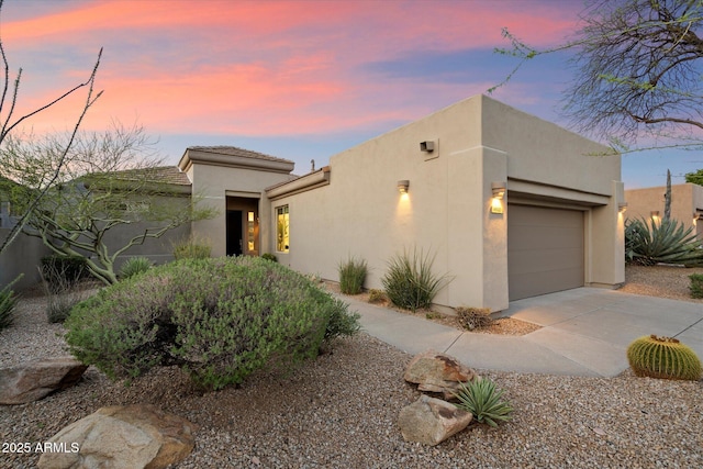 pueblo revival-style home featuring stucco siding, an attached garage, and concrete driveway