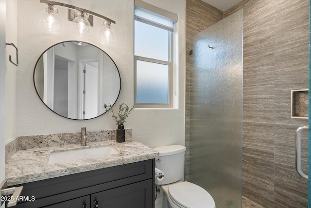 full bathroom with vanity, a textured wall, toilet, and tiled shower
