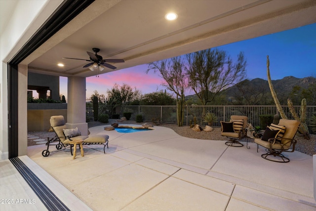 patio terrace at dusk featuring ceiling fan, fence, and a mountain view