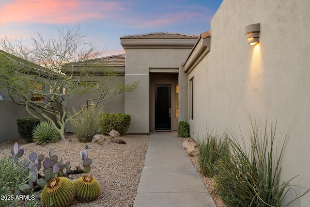 exterior entry at dusk with stucco siding and a tile roof