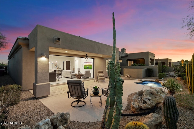 back of house at dusk with fence, stucco siding, an outdoor living space, and a patio area