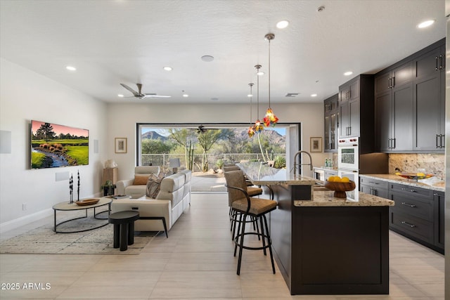 kitchen with a kitchen island with sink, a wealth of natural light, light stone counters, and decorative backsplash