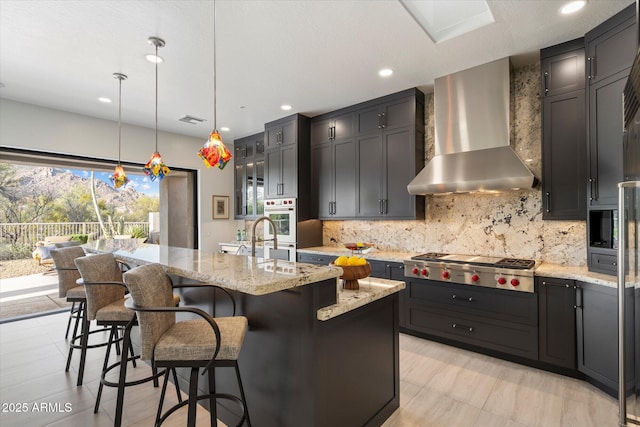 kitchen with visible vents, stainless steel gas cooktop, wall chimney exhaust hood, tasteful backsplash, and light stone counters