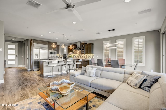 living room with baseboards, visible vents, a ceiling fan, light wood-type flooring, and recessed lighting