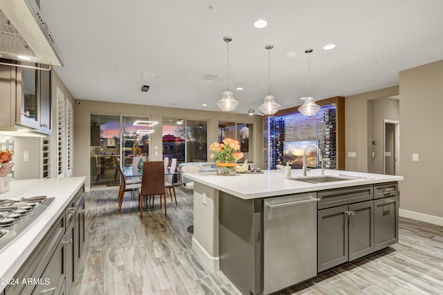 kitchen with decorative light fixtures, gray cabinets, light countertops, a kitchen island with sink, and a sink