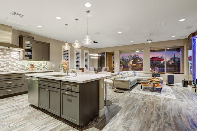 kitchen with a center island with sink, wall chimney exhaust hood, glass insert cabinets, light countertops, and a sink