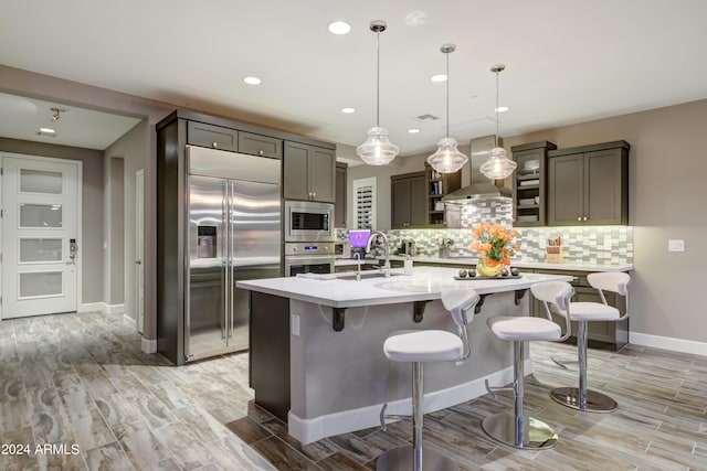 kitchen with light countertops, hanging light fixtures, wall chimney exhaust hood, and built in appliances