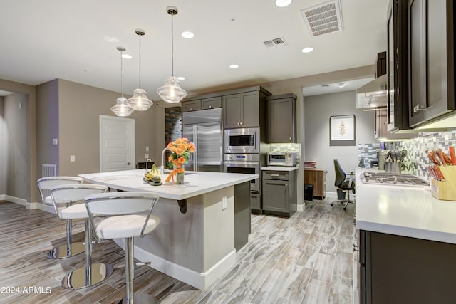 kitchen featuring pendant lighting, a center island with sink, light countertops, visible vents, and built in appliances