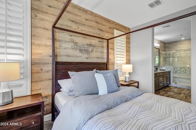 bedroom featuring connected bathroom, wooden walls, visible vents, and wood finished floors