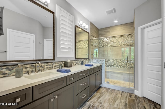 full bath featuring wood finish floors, a sink, a tile shower, and double vanity