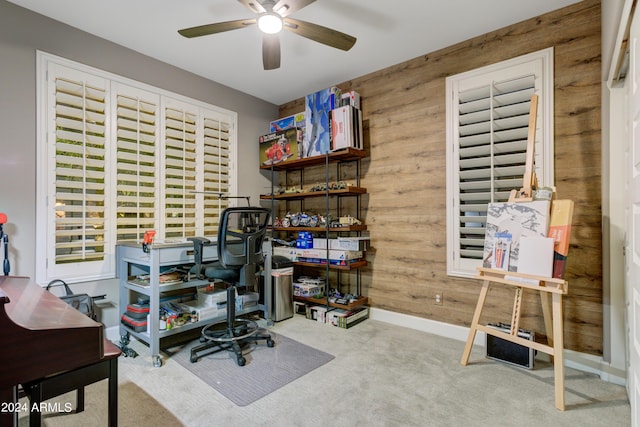 carpeted office space featuring wood walls, a ceiling fan, and baseboards