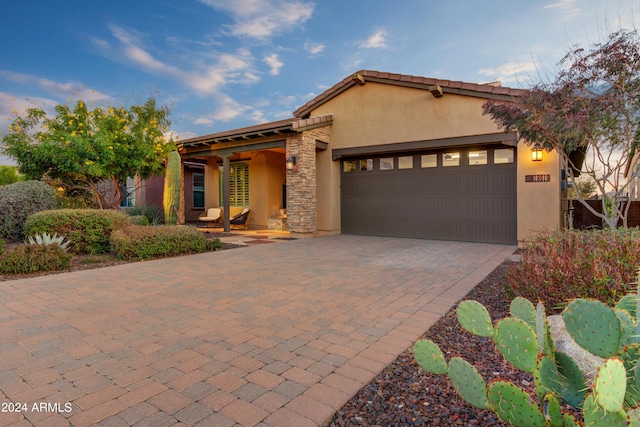 view of front facade featuring a garage, stone siding, decorative driveway, and stucco siding