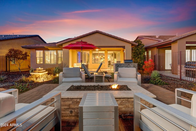 back of property at dusk featuring a patio area, an outdoor fire pit, fence, and stucco siding