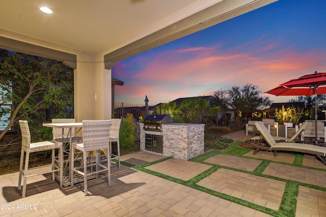 patio terrace at dusk with fence, an outdoor bar, and area for grilling