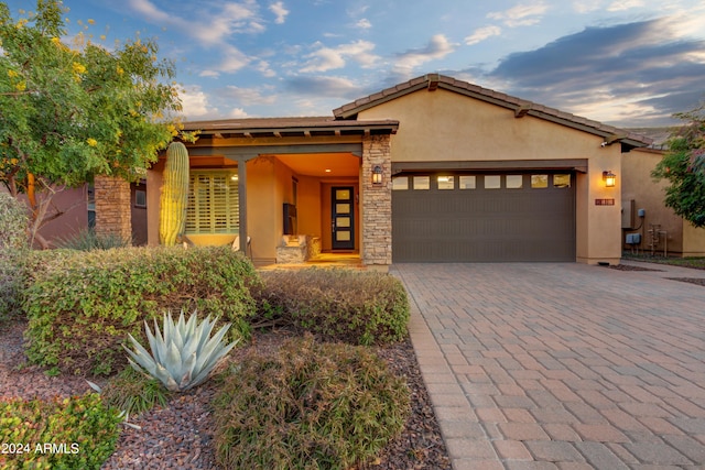 view of front of home featuring an attached garage, stone siding, decorative driveway, and stucco siding