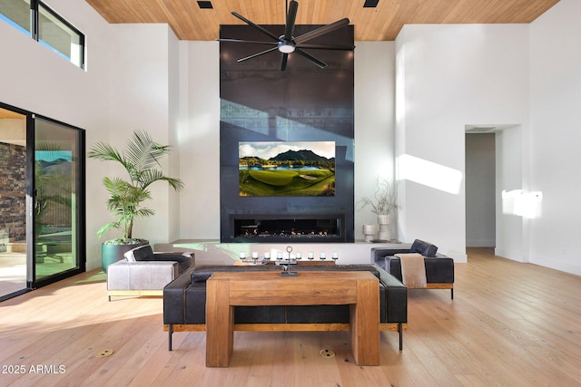 living room featuring light hardwood / wood-style floors, a towering ceiling, wooden ceiling, and a large fireplace