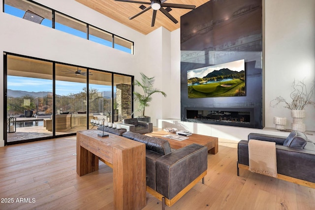 living room with a mountain view, a fireplace, ceiling fan, and light wood-type flooring