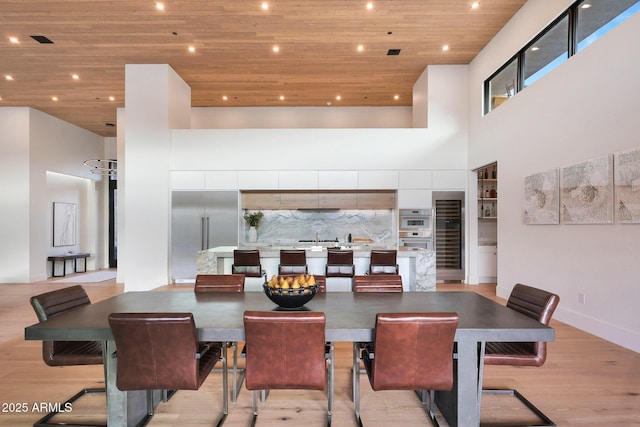 dining space featuring wood ceiling, light hardwood / wood-style flooring, and a high ceiling