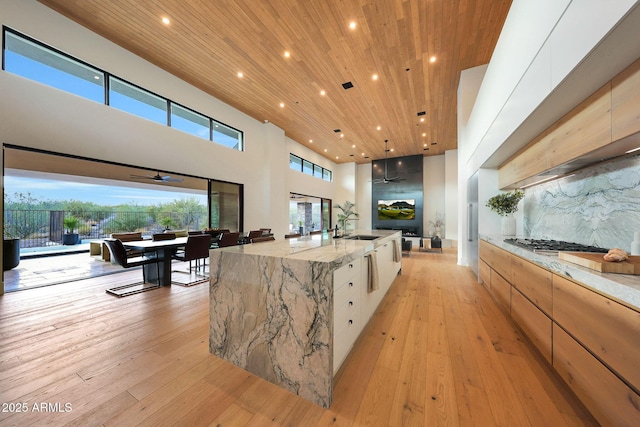 kitchen with a large island, light hardwood / wood-style flooring, light stone countertops, white cabinets, and wooden ceiling